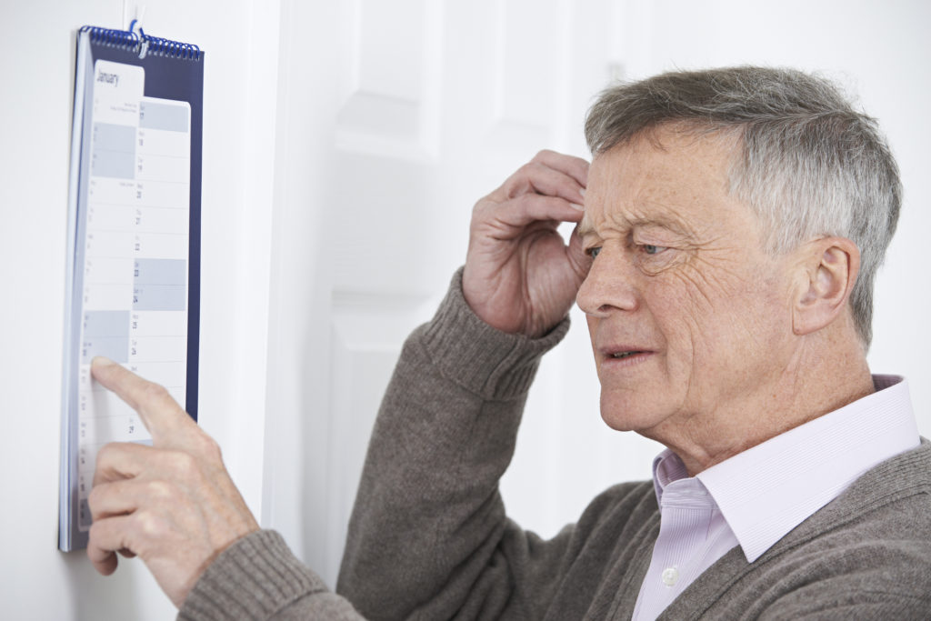 Confused Senior Man With Dementia Looking At Wall Calendar