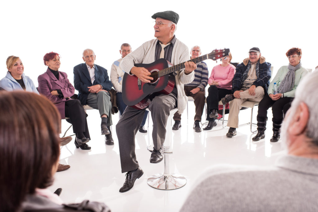 Large group of seniors enjoying in social gathering. Senior man is playing a guitar. Isolated on white.