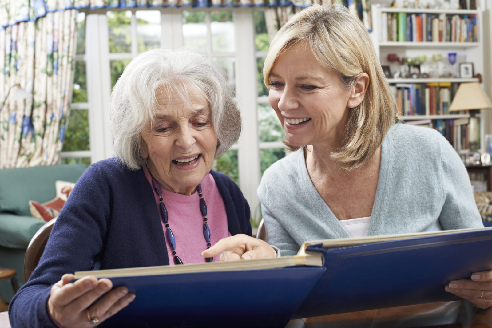 daughter sitting with elderly mother with dementia looking at photo album