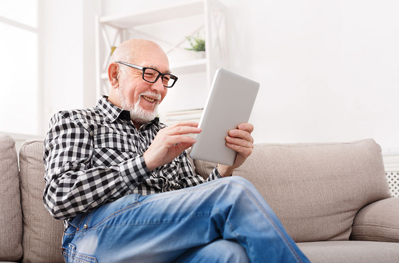 senior man sitting on couch looking at computer tablet