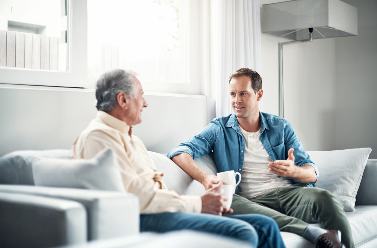 adult son talking with elderly father on living room couch