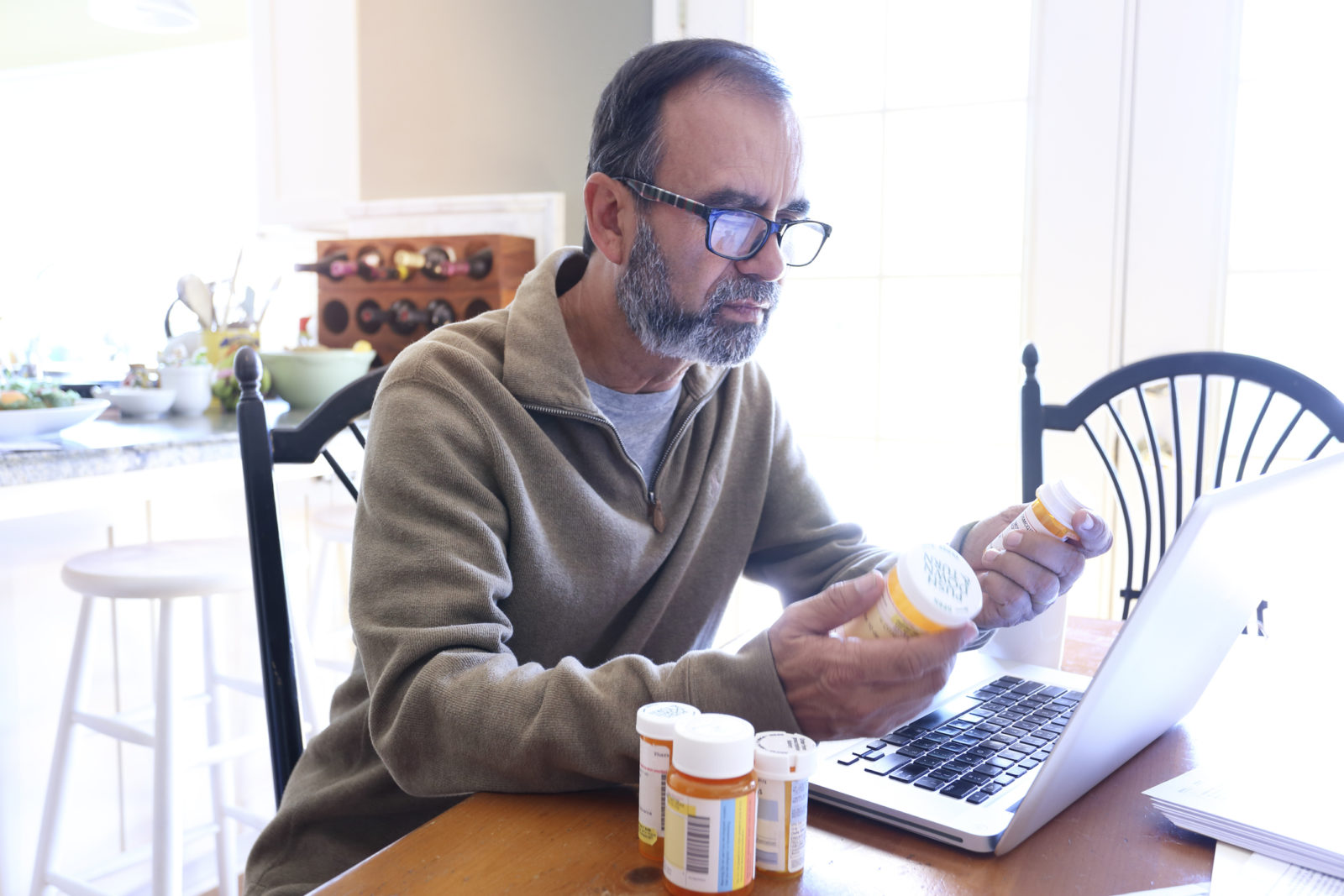 elderly man looking at pill bottles in front of computer