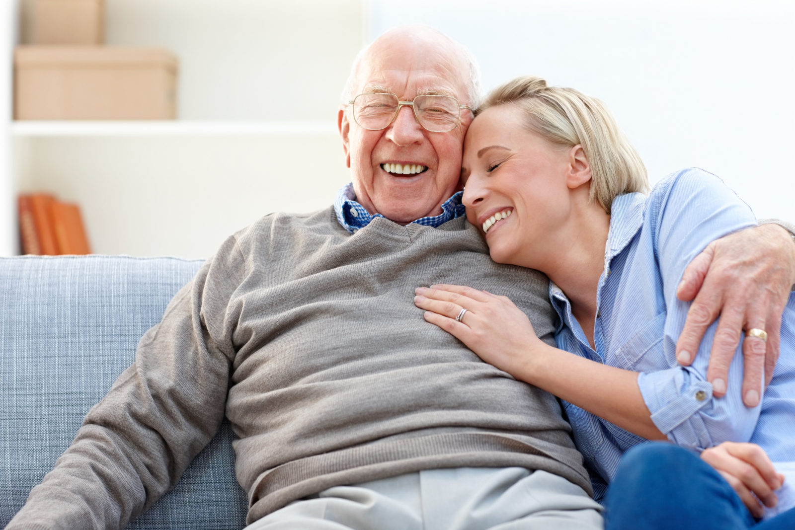 Loving senior man embracing his adult daughter while sitting on sofa smiling