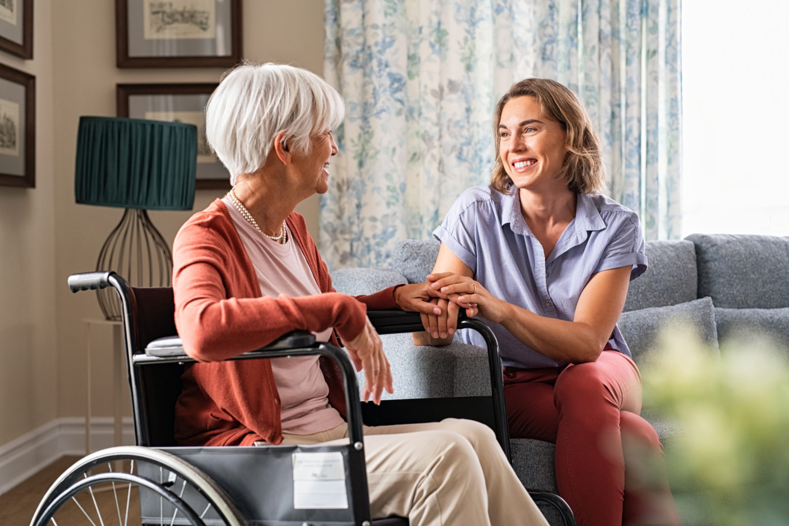 Mature woman comforting senior woman sitting on wheelchair at nursing home.