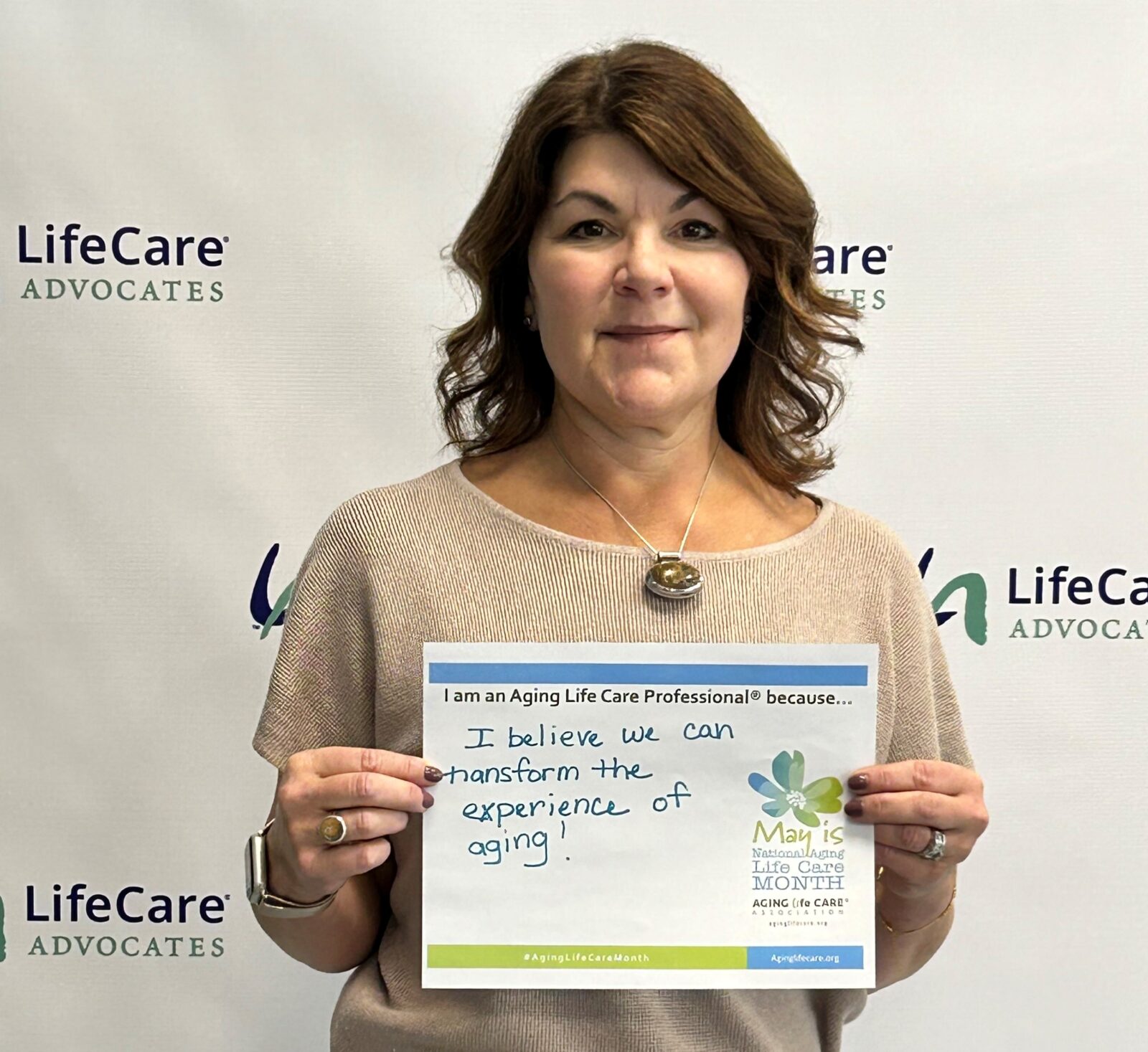 Picture of Kate Granigan holding a sign that says, "I believe we can transform the experience of aging!"