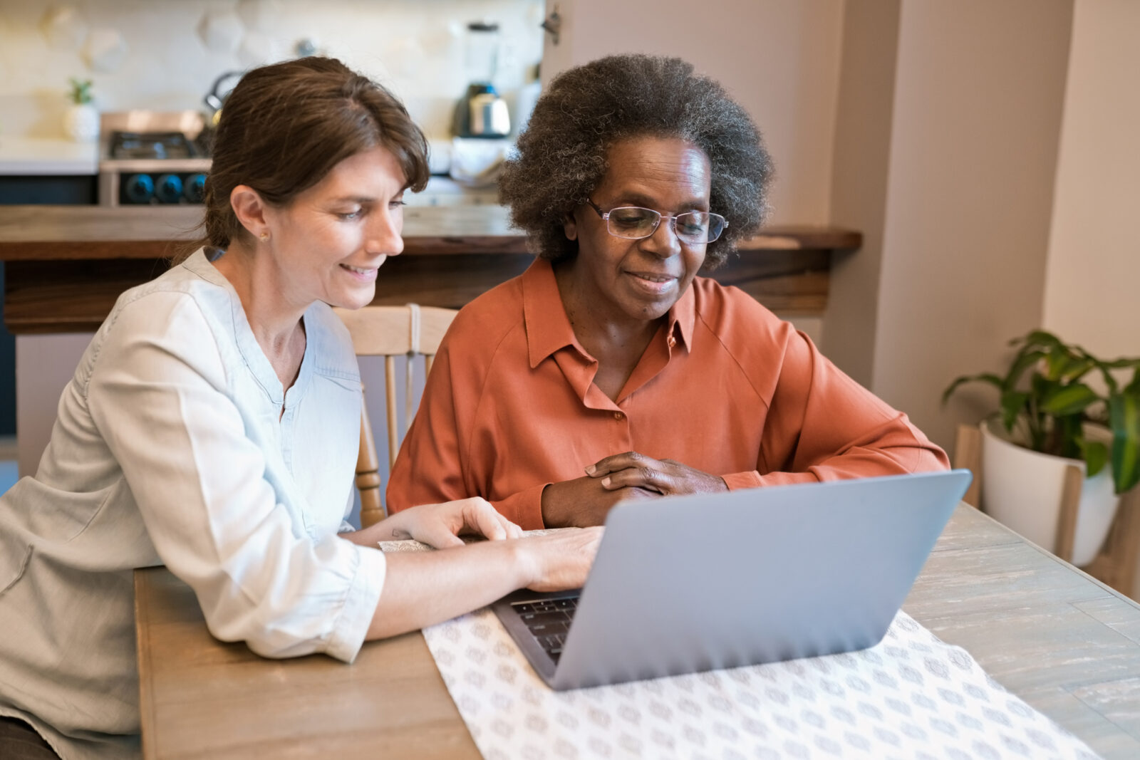 Smiling caregiver teaching laptop skills to senior woman.