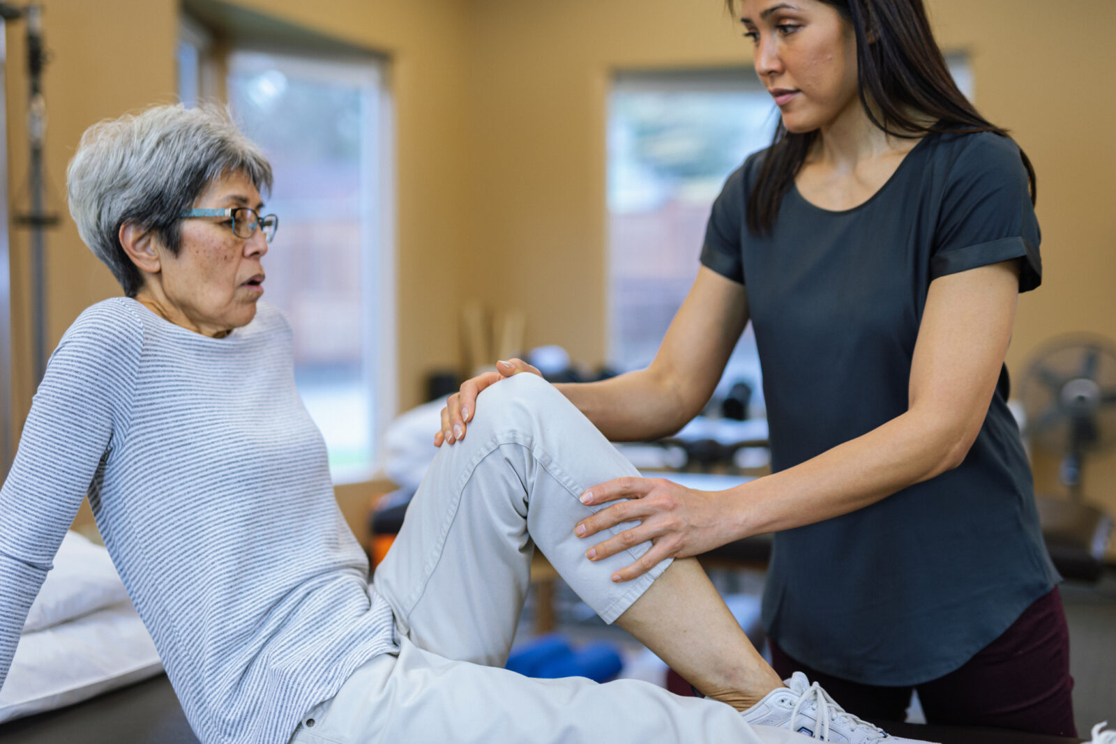Physical therapist holds the knee of a senior female patient as they work on improving leg strength and mobility.