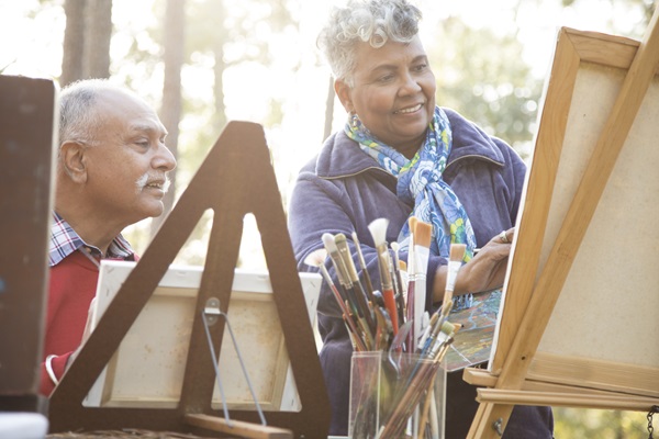 Mixed race, active senior adult couple enjoys art hobby together outdoors in public park or forest area. Or instructor and student taking art lessons. African and Indian ethnicities.